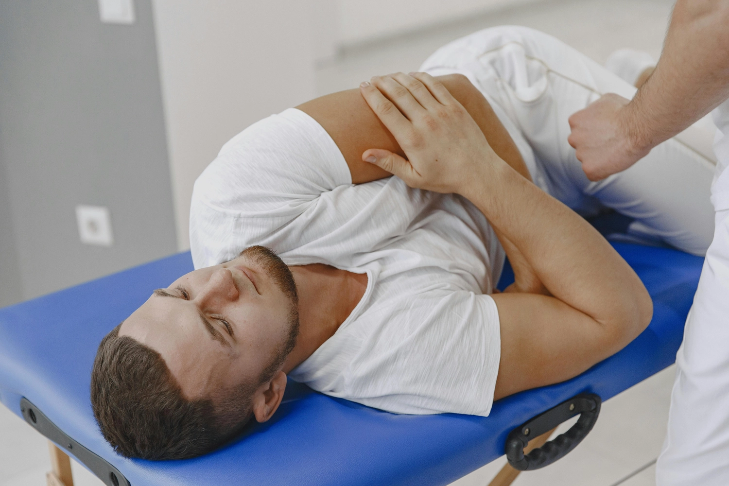 Praxis für Chiropraktik - Therapien und Behandlungs - Ein junger Mann liegt auf einer blauen Behandlungsliege und erhält von einem Therapeuten eine physiotherapeutische oder chiropraktische Behandlung.
