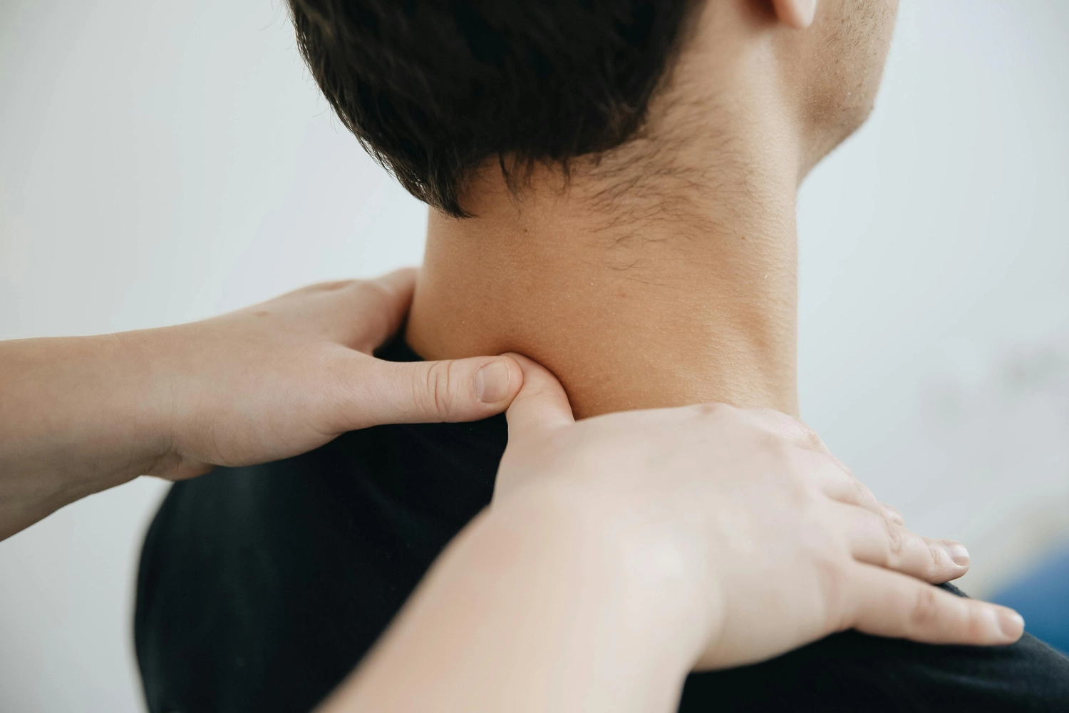Praxis für Chiropraktik - Therapien und Behandlungs - Rückansicht eines männlichen Therapeuten, der einem männlichen Patienten im Krankenhaus eine Nackenmassage gibt.