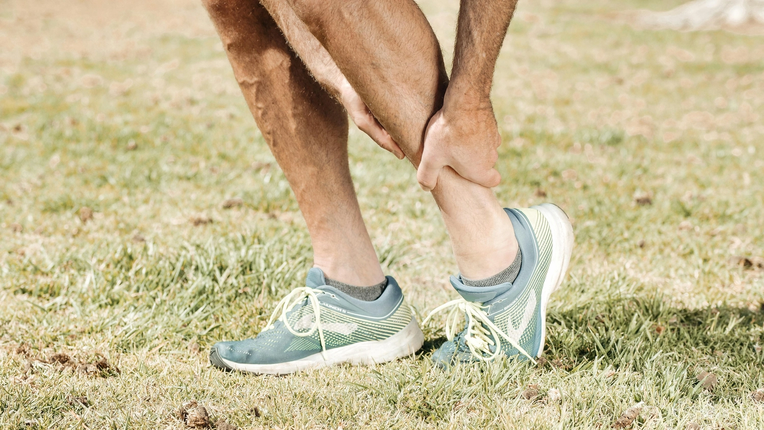 Praxis für Chiropraktik - Therapien und Behandlungs - Ein männlicher Läufer hält sich die verletzte Wade und leidet unter Schmerzen. Bänderzerrung beim Laufen im Freien. Nahaufnahme der Beine.